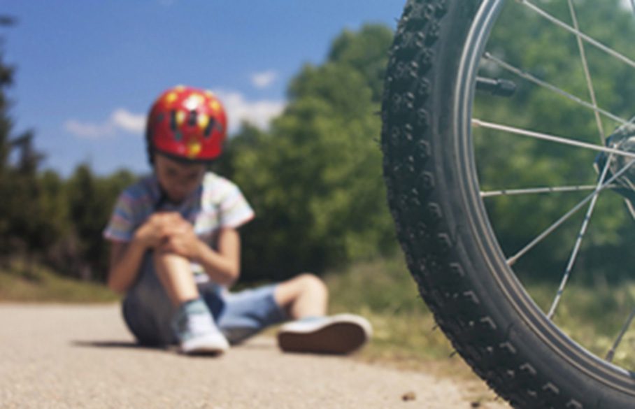 Barn har veltet med sykkel og sitter på bakken med skrubbsår på kneet.